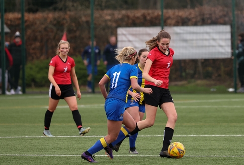 action shot of women playing football. Player with red has ball and player with blue is going in to tackle 