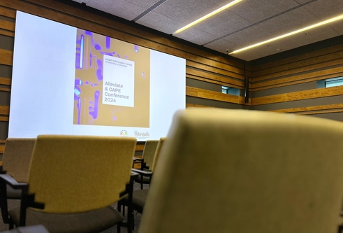 A powerpoint side showing the conference title on a screen in an empty room