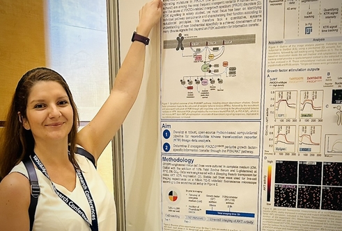 woman in white t-shirt and lanyard pointing at scientific poster