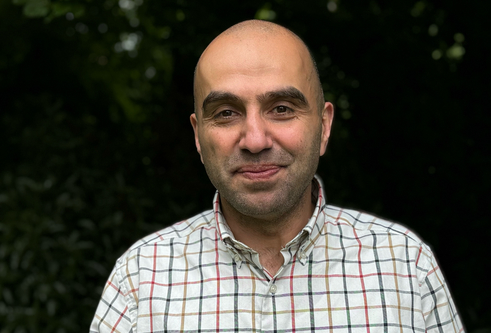 Profile shot of Professor Husam AlWaer. He is smiling and wearing a checkered shirt.