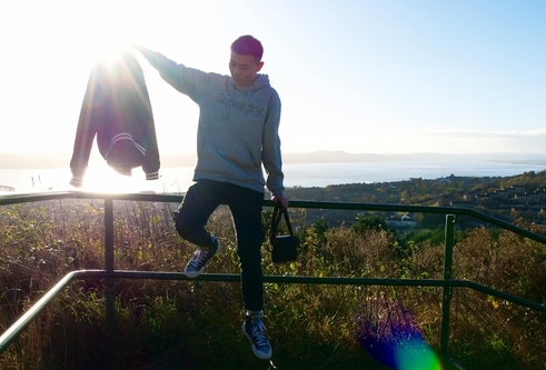 A man sits on metal railing overlooking a viewpoint above the city of Dundee, with the river in the background