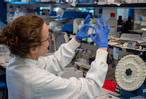 woman in lab wearing a lab coat and blue latex gloves holding up a vile