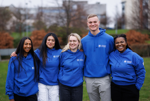 Five student sin blue uni jumpers stood together in a row smiling