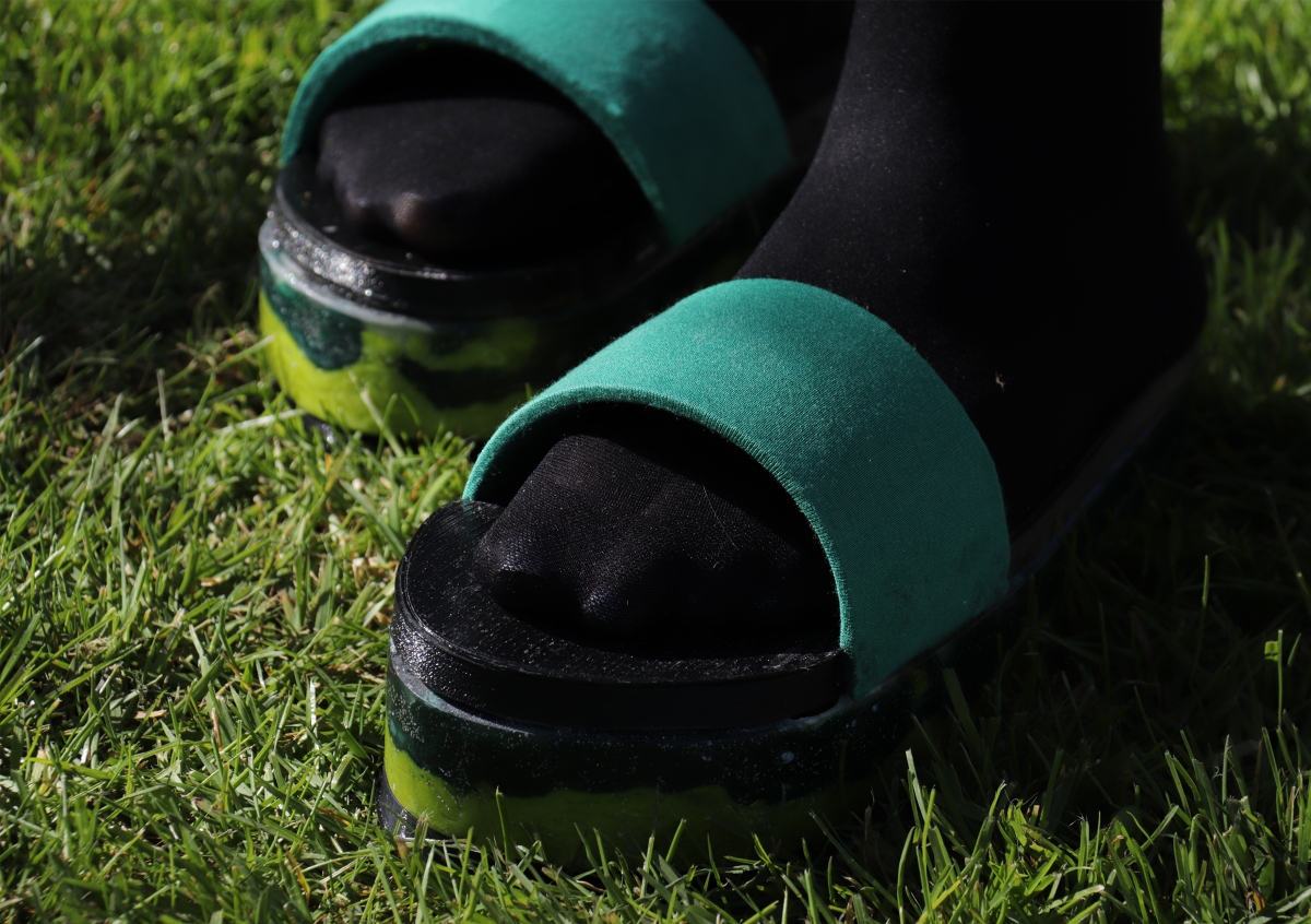Black and green slider shoes, being worn on grass. Shin to foot shown.