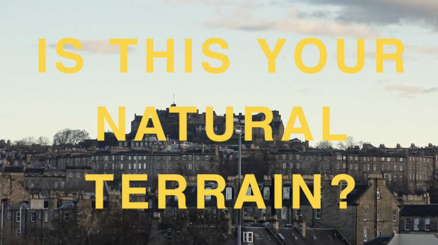 A screenshot taken from a moving image. An image of Edinburgh's skyline, including Tenement homes and Edinburgh Castle on an autumnal day is layered with yellow text in capital letters which reads, 'IS THIS YOUR NATURAL TERRAIN?'