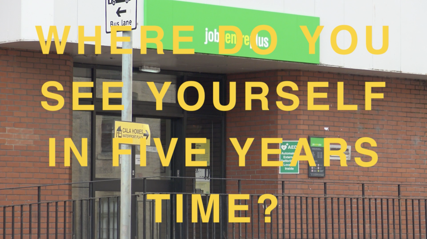 A screenshot taken from a moving image. An image of a red brick building which is a Job Centre is layered with yellow text in capital letters which reads, 'WHERE DO YOU SEE YOURSELF IN FIVE YEARS TIME?'