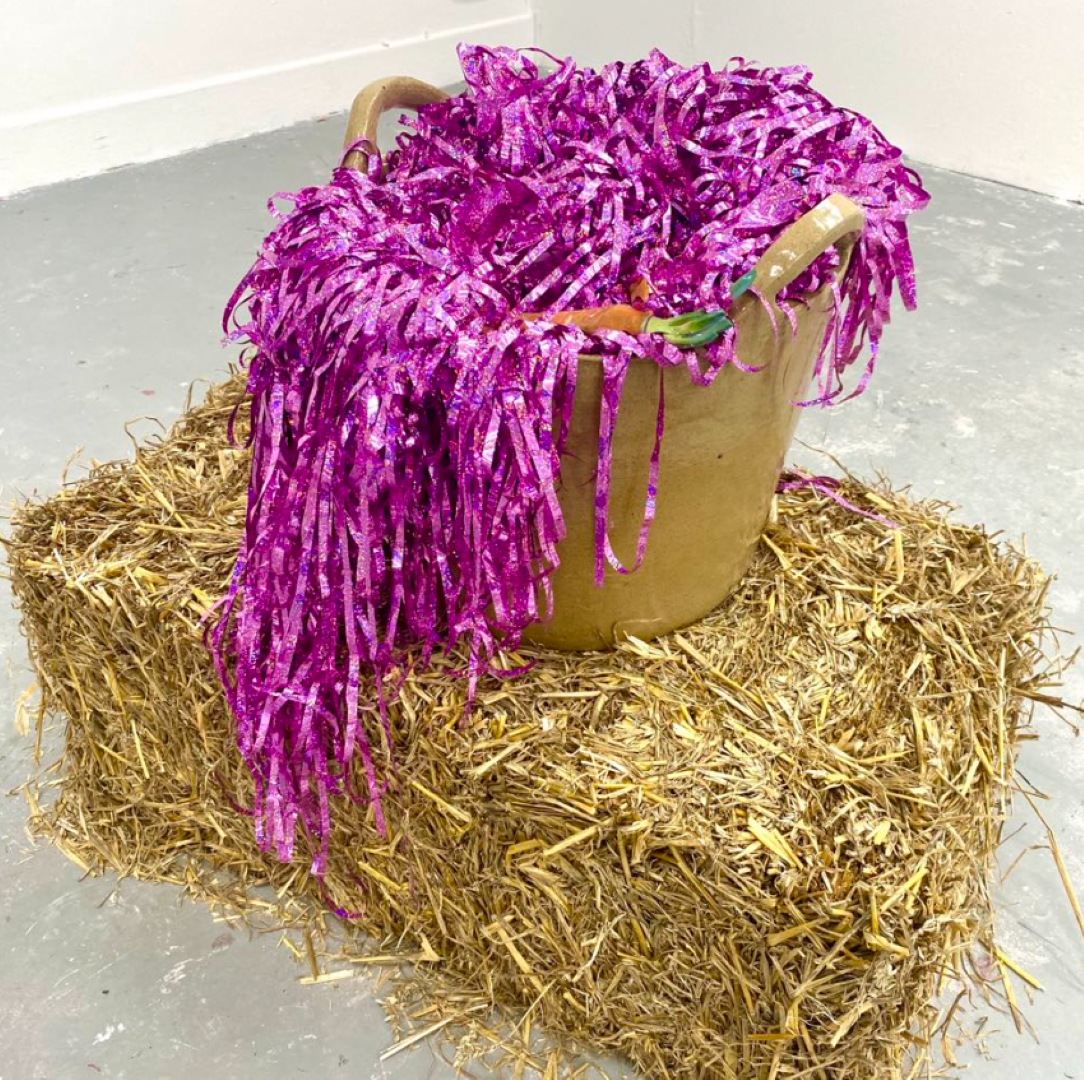 Ceramic bucket on a bale of straw. The bucket is filled with ceramic carrots and sparkly streamers.